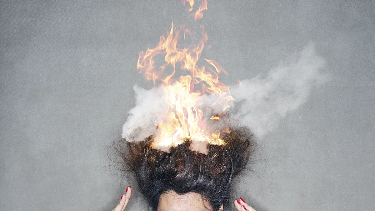 A top of the woman's head on a gray background wth her hair on fire